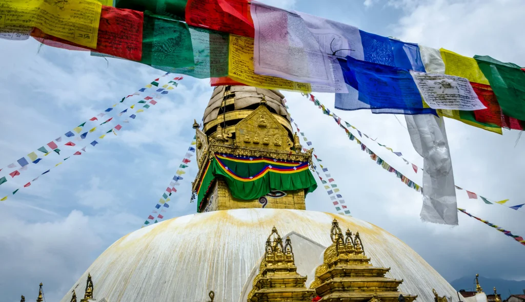 White domed stupa topped with golden spire and vibrant prayer flags fluttering against the sky in the Kathmandu Valley.