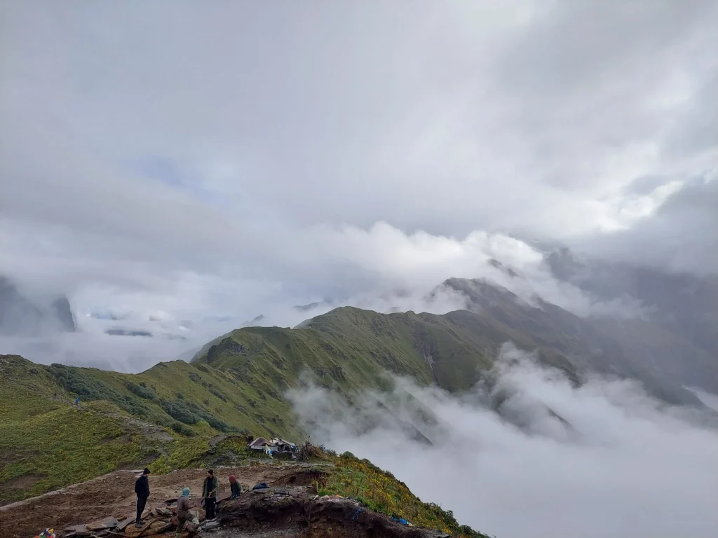 People standing on a high green ridge overlooking mountain ranges wrapped in clouds.