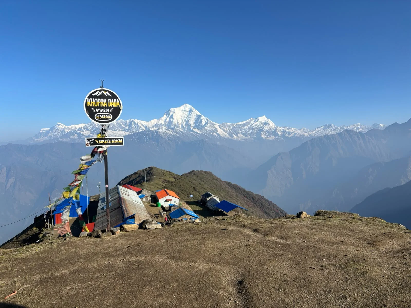 Khopra Danda Trek-12 Days Khopra Danda trek viewpoint at 3,660 meters with mountain lodges, prayer flags, and panoramic snow-capped Himalayan peaks in Nepal.