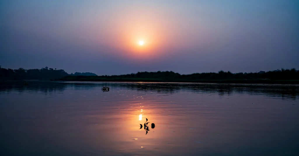 Things to do in chitwan include watching a tranquil sunset cast golden reflections over the calm river waters near the national park.
