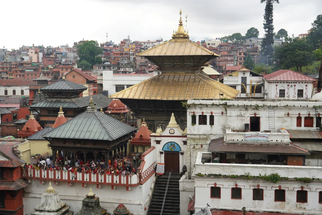 Sacred pagoda-style temple complex with distinctive golden roofs and crowds of devotees in the Kathmandu Valley.
