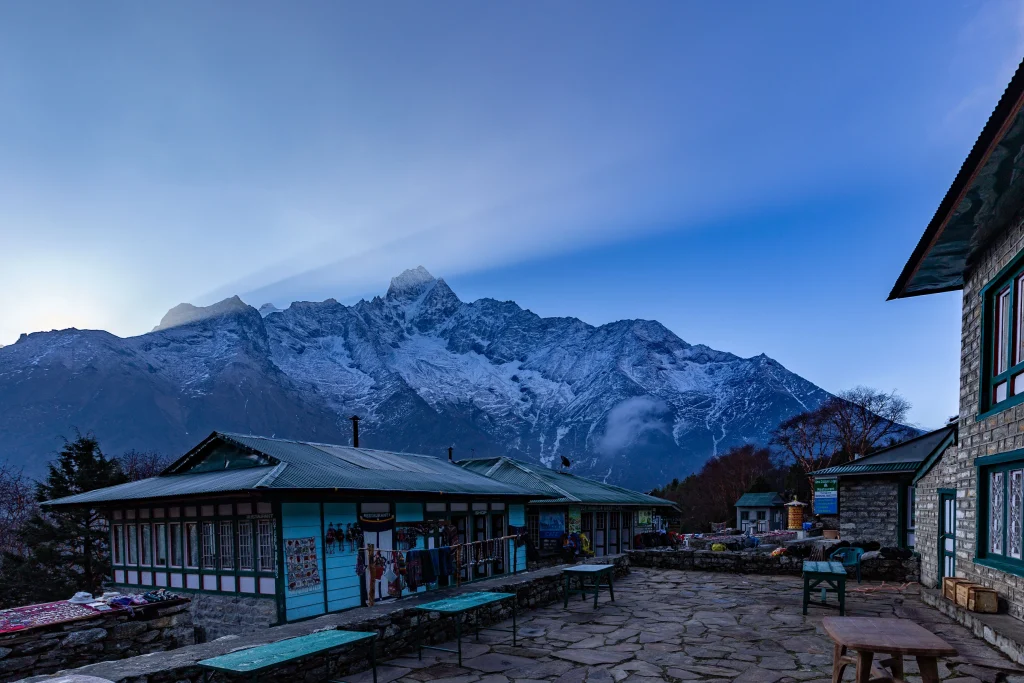 Mountain lodge buildings with a stone courtyard and towering snow-covered peaks in the background.