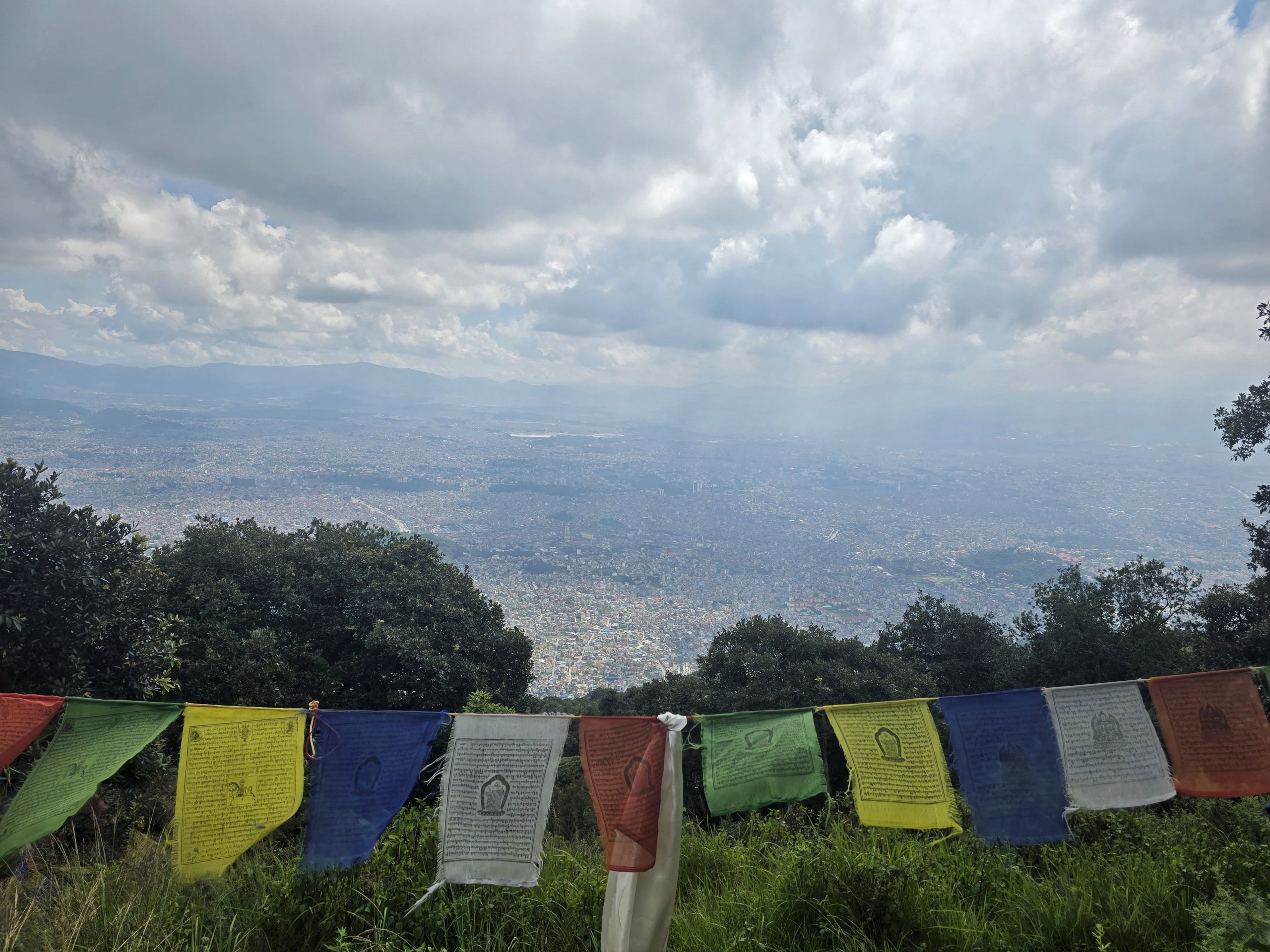 Panoramic view of Kathmandu Valley and colorful Buddhist prayer flags from the Jamacho viewpoint on a one-day hiking trip.