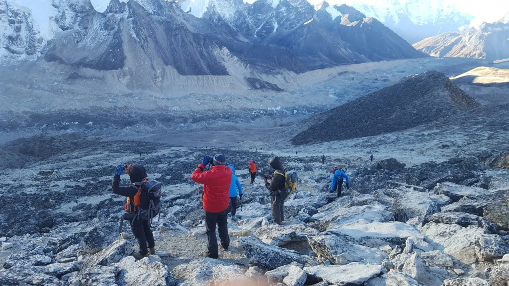 A group of hikers with backpacks navigating a rugged, rocky mountain slope overlooking a glacial valley on the everest base camp trek.