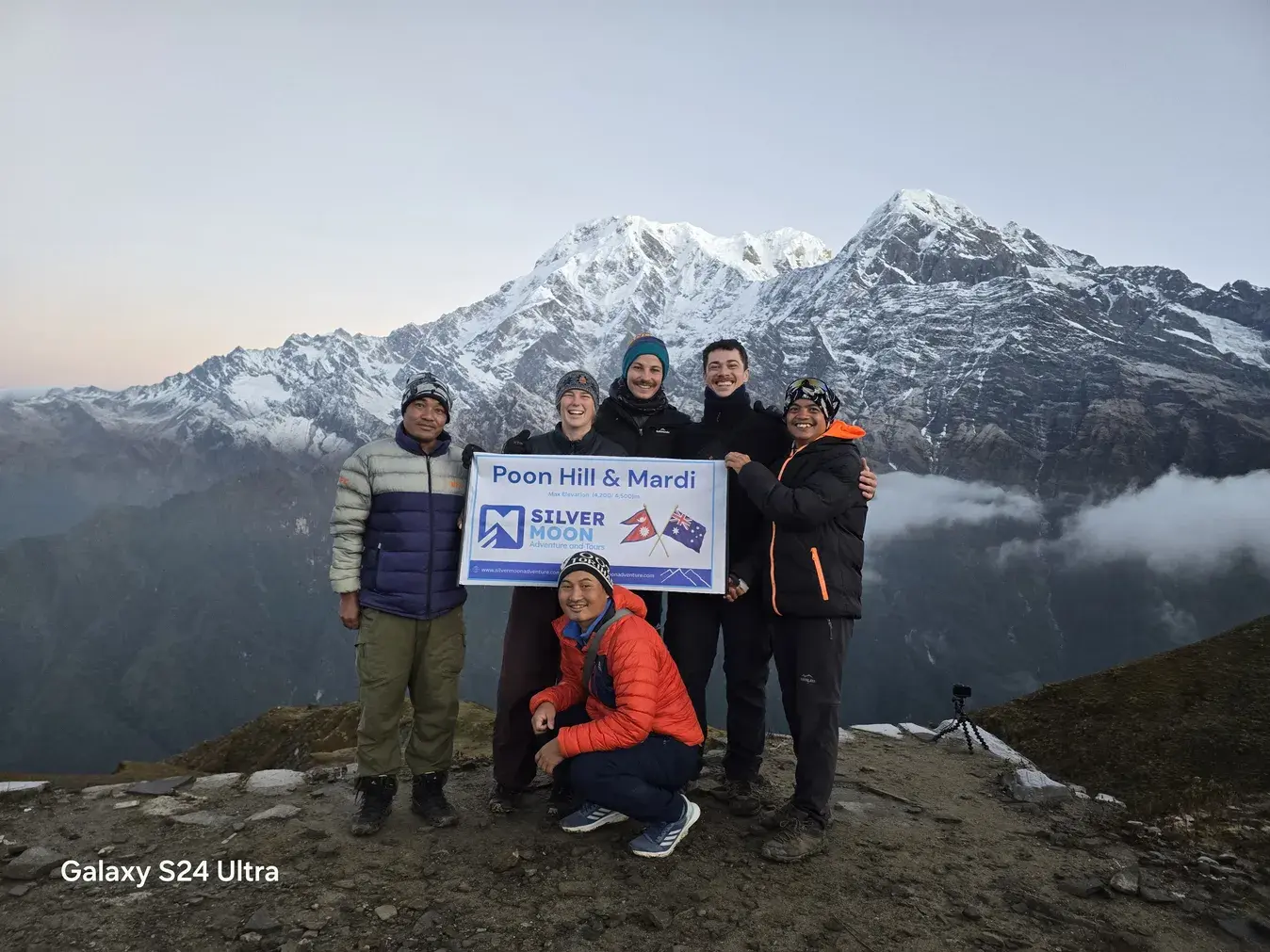 Mardi Himal Trek from Pokhara – 6 Days Silver Moon Adventure trekking team and Australian clients holding a company banner at a Himalayan viewpoint during the Poon Hill and Mardi Himal trek, with snow-covered Annapurna mountains in the background.