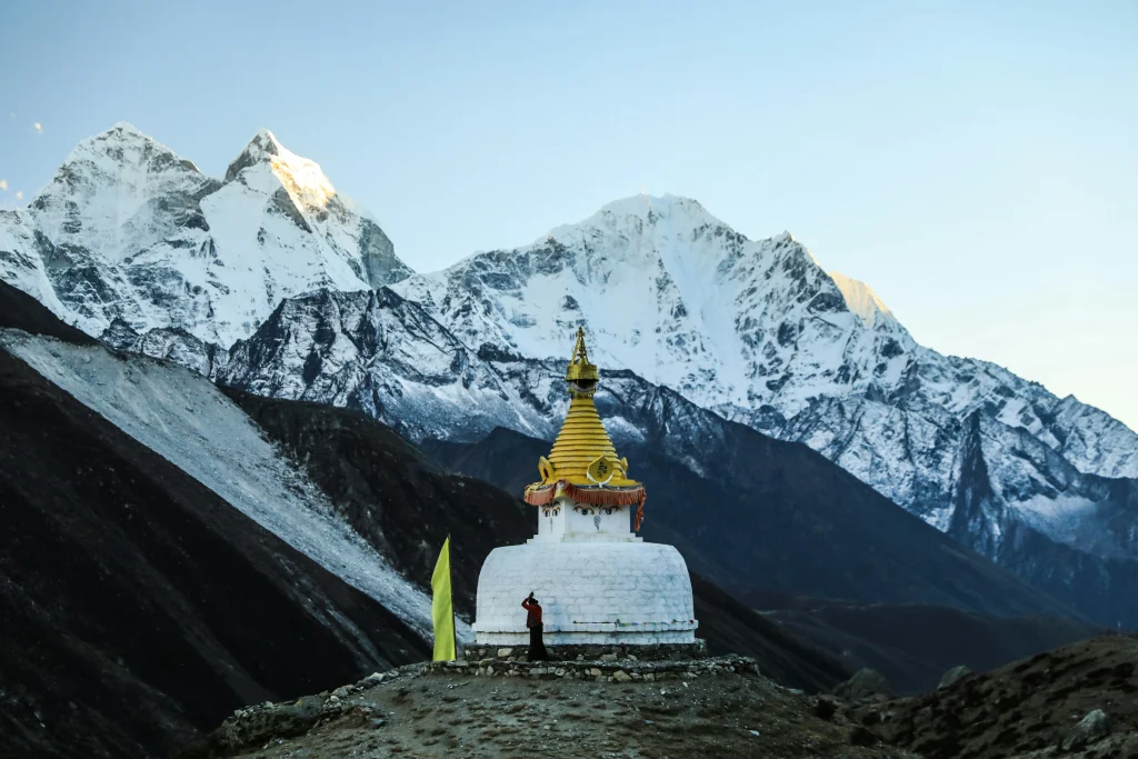 A white Buddhist stupa with a golden spire standing on a mountain ridge in front of massive snow-dusted Himalayan peaks along the everest base camp trek.