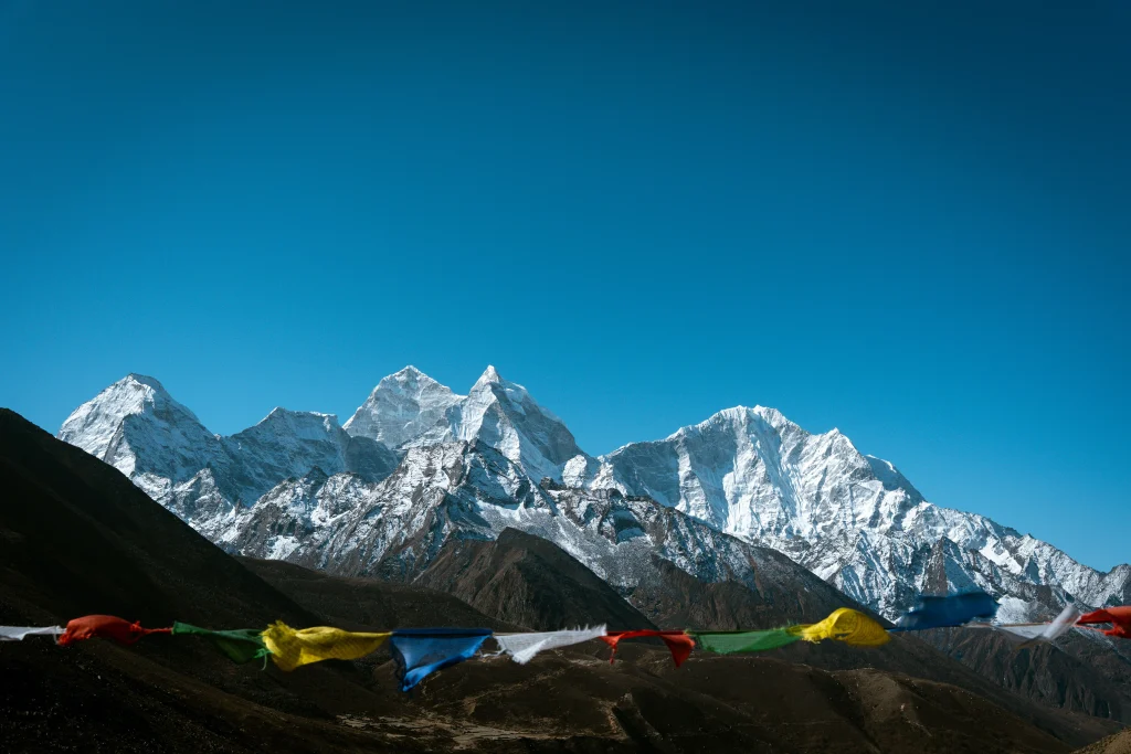 Colorful Buddhist prayer flags stretched across the foreground in front of majestic, snow-covered mountain peaks along the everest base camp trek.