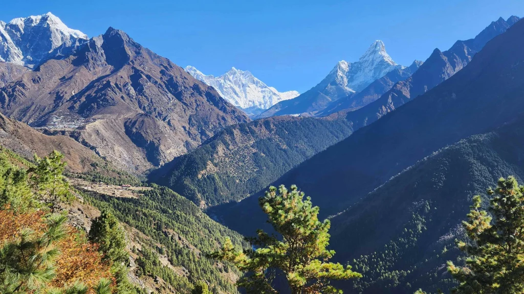 A wide panoramic view of steep green pine valleys framing Mount Everest and the distinct pyramid peak of Ama Dablam on the everest base camp trek.