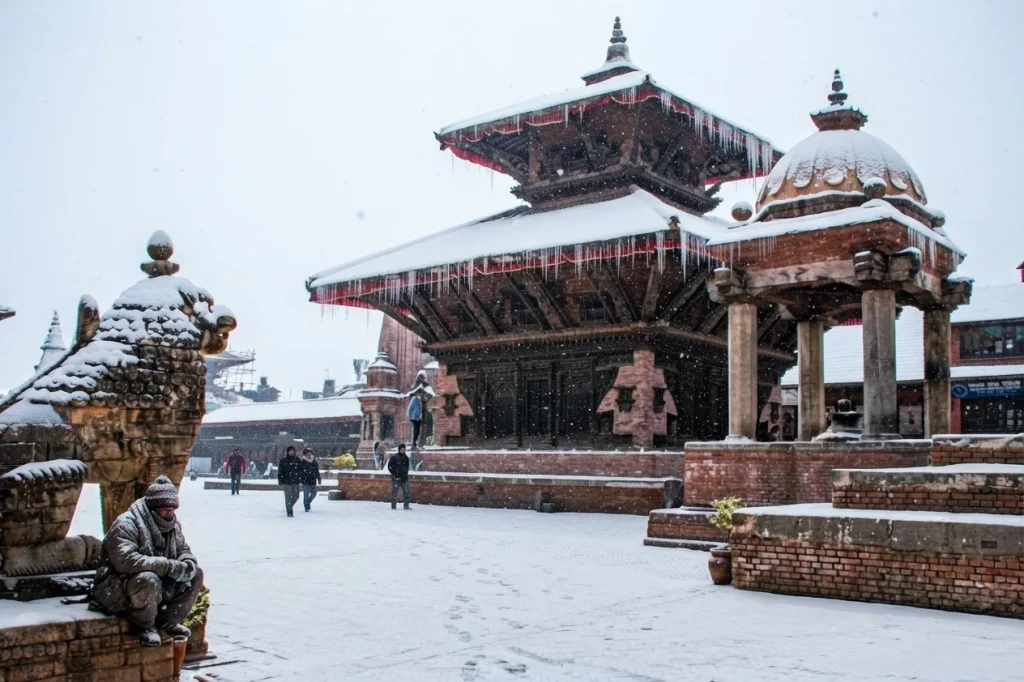 People walking through Bhaktapur Durbar Square amidst a scenic winter snowfall.