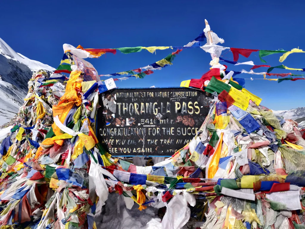 The iconic Thorong La Pass signboard at 5,416 meters draped in colorful Buddhist prayer flags along the Annapurna Circuit trek.