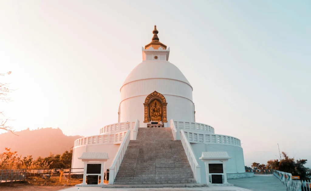 White dome of the World Peace Pagoda stupa in Pokhara with a central golden Buddha statue.