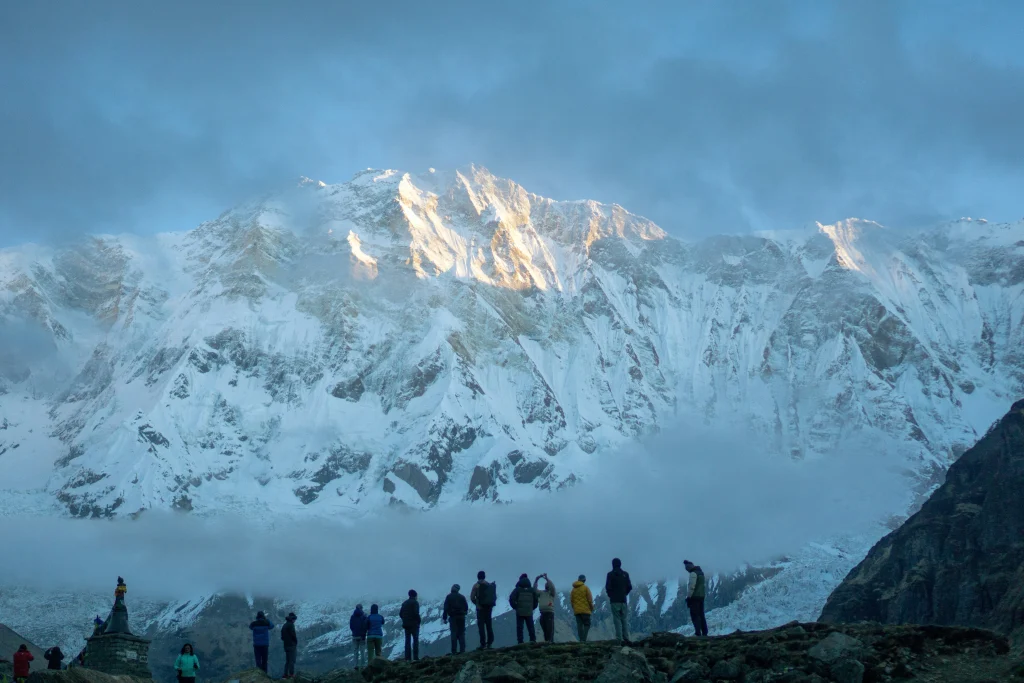 Silhouettes of trekkers standing on a high-altitude ridge watching the golden sunrise over a massive snow-capped mountain wall