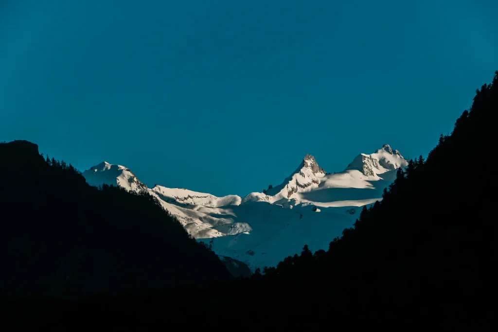 Dramatic view of snow-capped Himalayan peaks illuminated by sunlight between dark mountain silhouettes along the Manaslu Circuit.