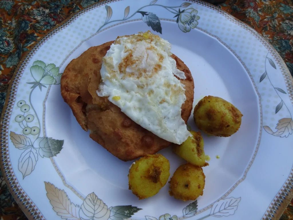 a plate featuring Tibetan fried bread topped with a fried egg and served with spiced potatoes.