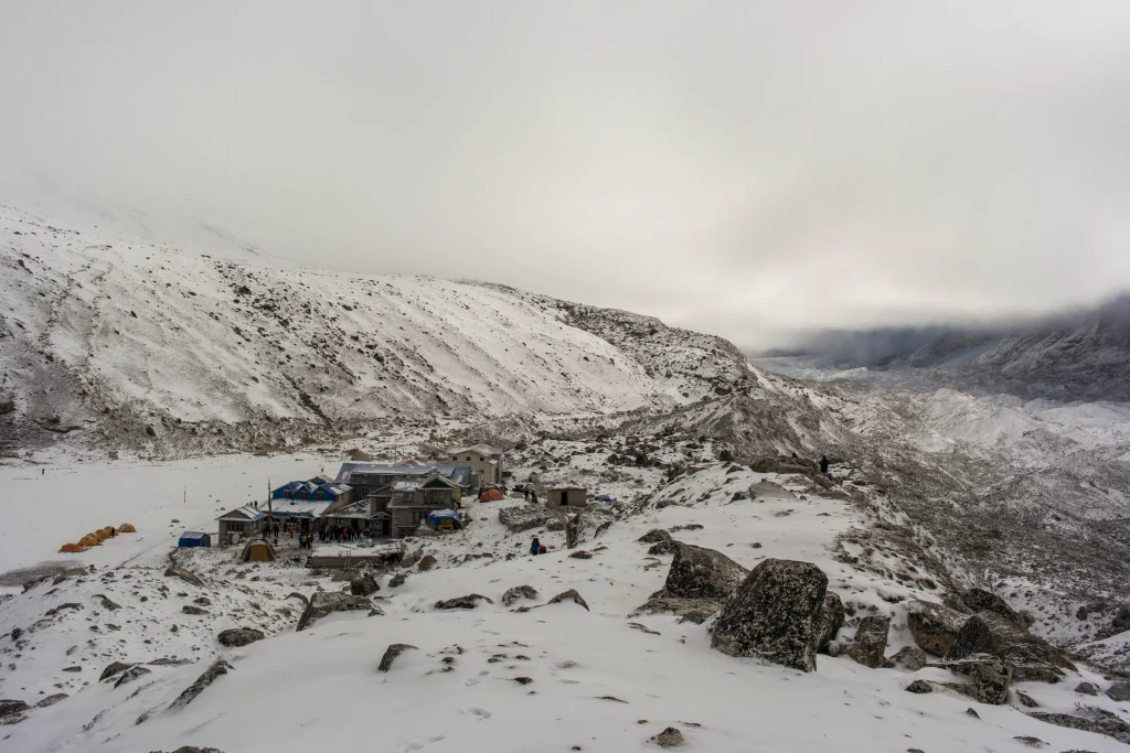 A remote, snow-draped teahouse settlement and yellow tents resting on a frozen mountain landscape along the everest base camp trek.