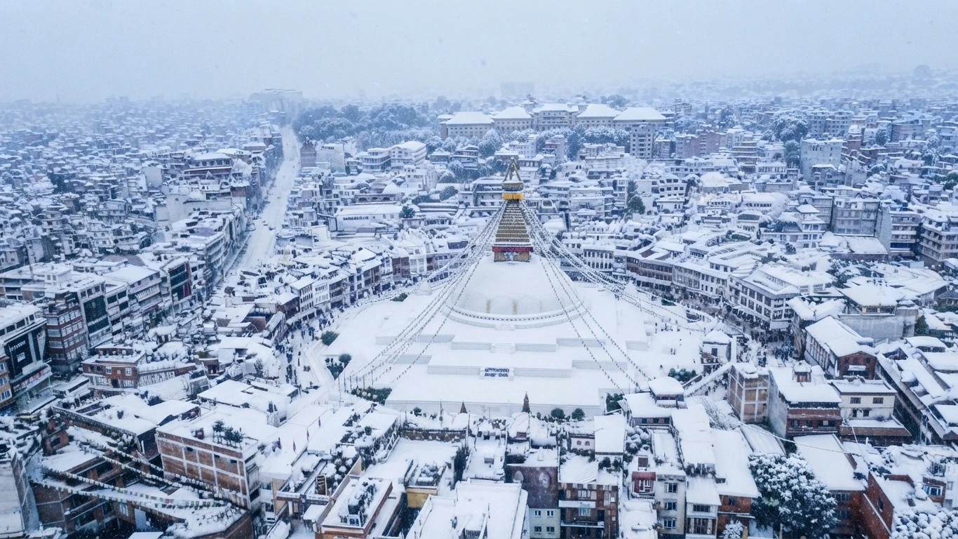 An aerial view of Boudhanath Stupa and surrounding city buildings covered in a fresh layer of winter snowfall.