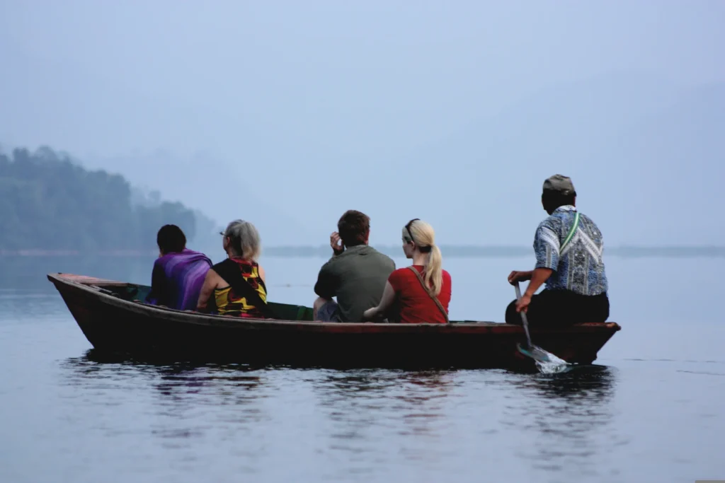 Tourists enjoying a calm wooden boat ride across Phewa Lake in Pokhara, Nepal.