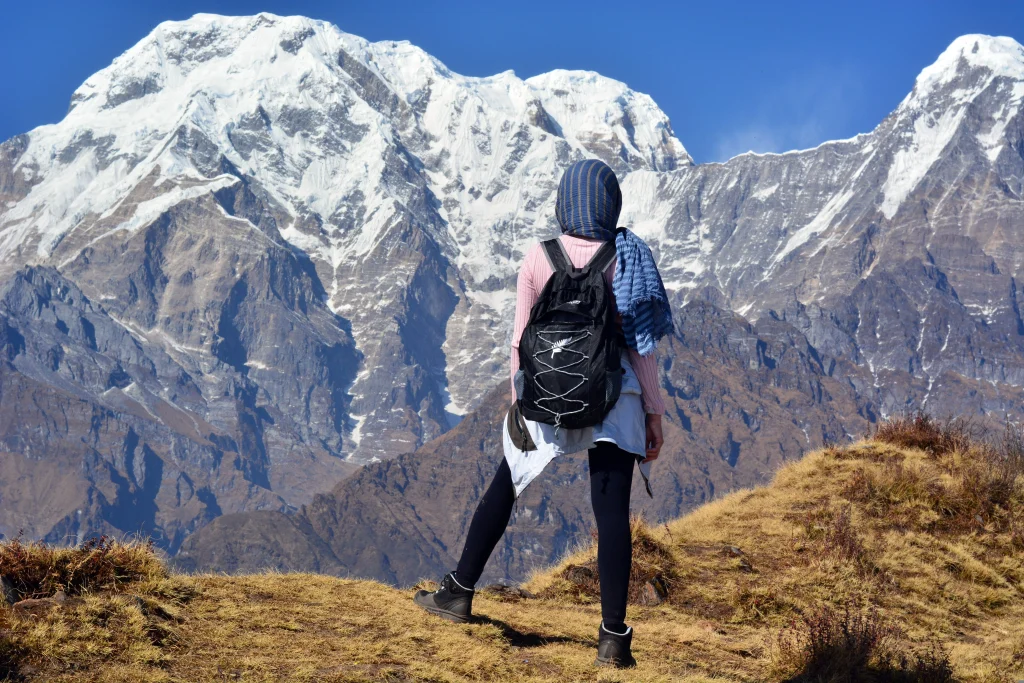 a hiker wearing a backpack taking in views of massive, snow-covered Himalayan peaks on a clear morning.