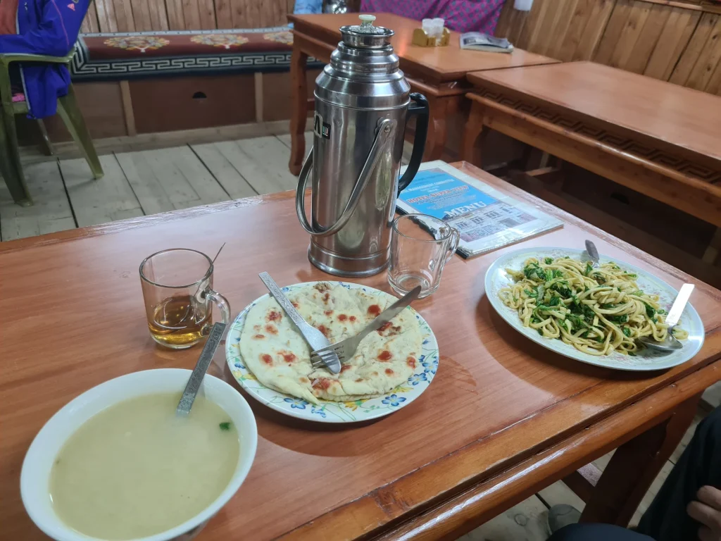 Freshly prepared Himalayan teahouse food including veg chow mein, flatbread, soup, and hot tea in a thermos flask.