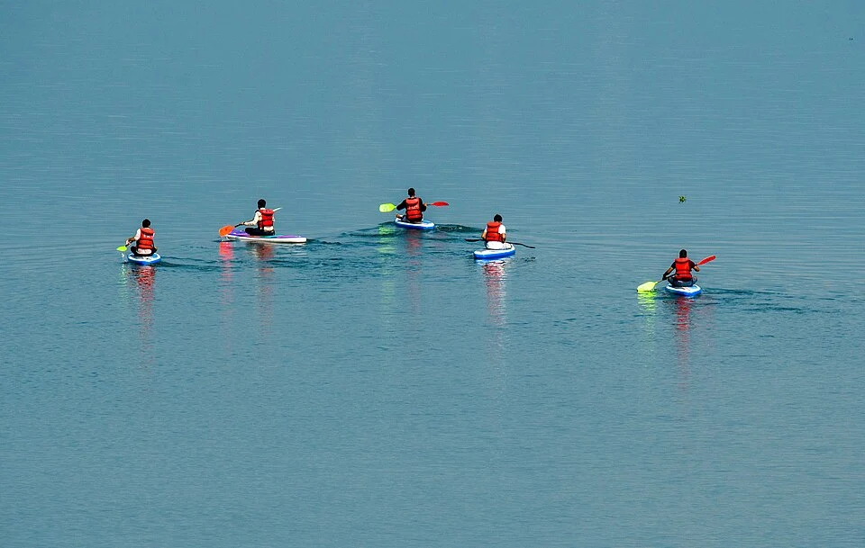 Group of people wearing life jackets kayaking and stand-up paddleboarding on calm waters in Pokhara