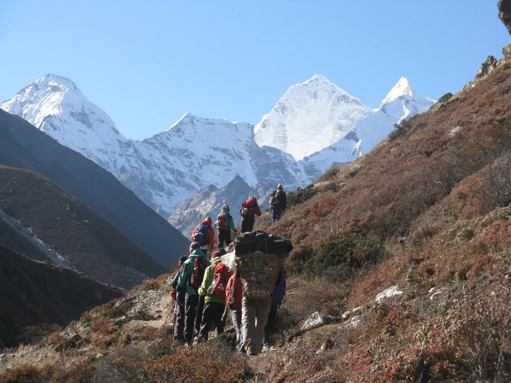 A line of hikers and porters trekking up a mountain path towards giant snow peaks during a standard vs luxury ebc trek.